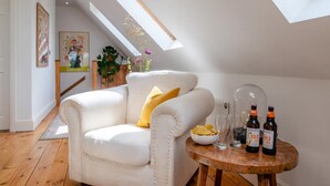 Una habitación acogedora con un sillón blanco, una mesita de madera con botellas y un tazón de papas fritas.