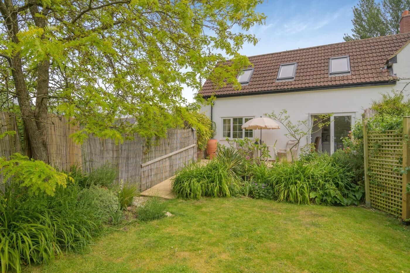 Ein Haus mit Garten, Holzzaun und einer Terrasse mit Tisch und Stühlen.