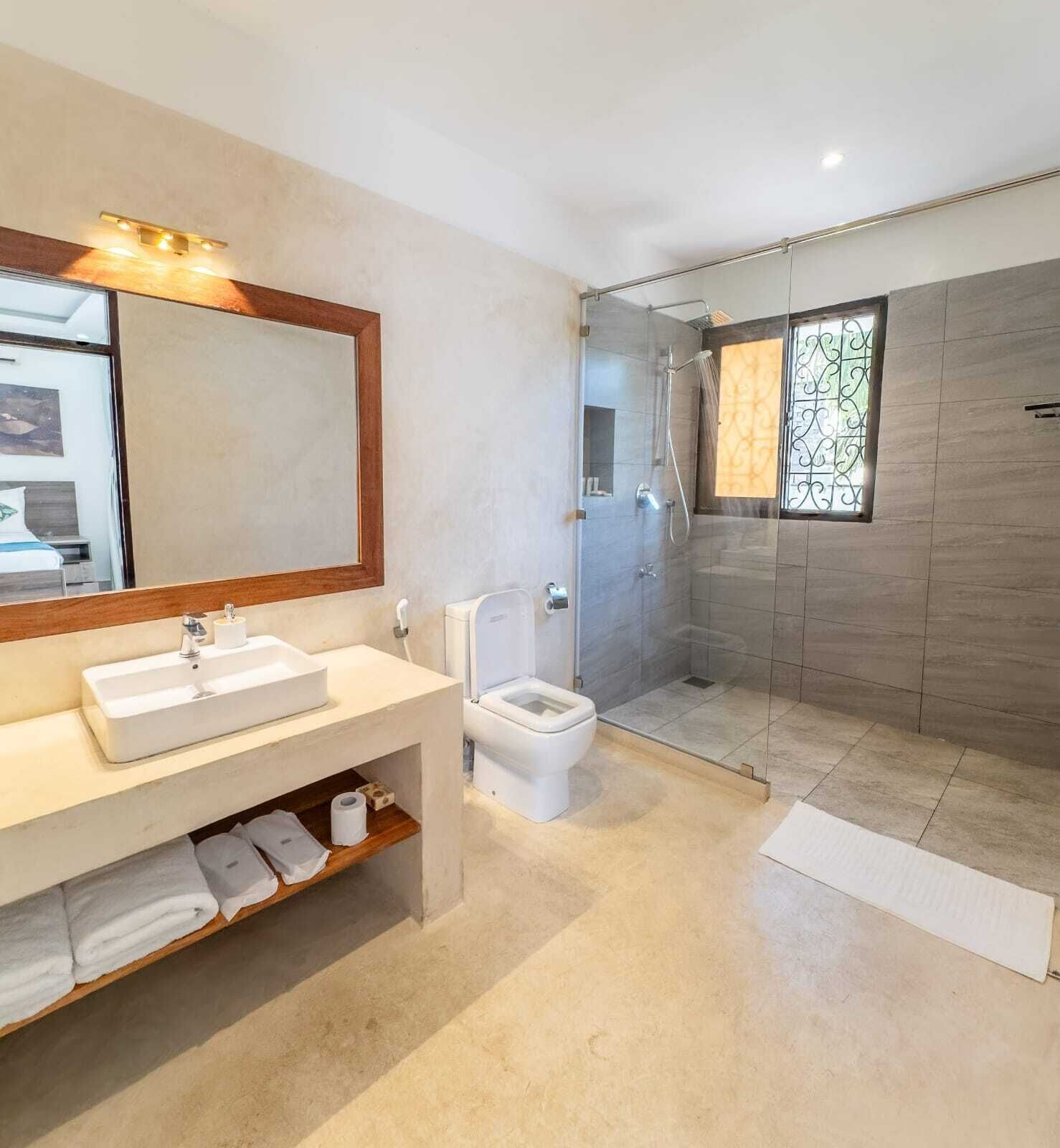 A modern bathroom with a large mirror, a sink, a toilet, and a shower area.