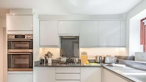 Ett modernt kök med vita skåp, en inbyggd ugn, en bänkskiva i granit och diverse köksredskap.