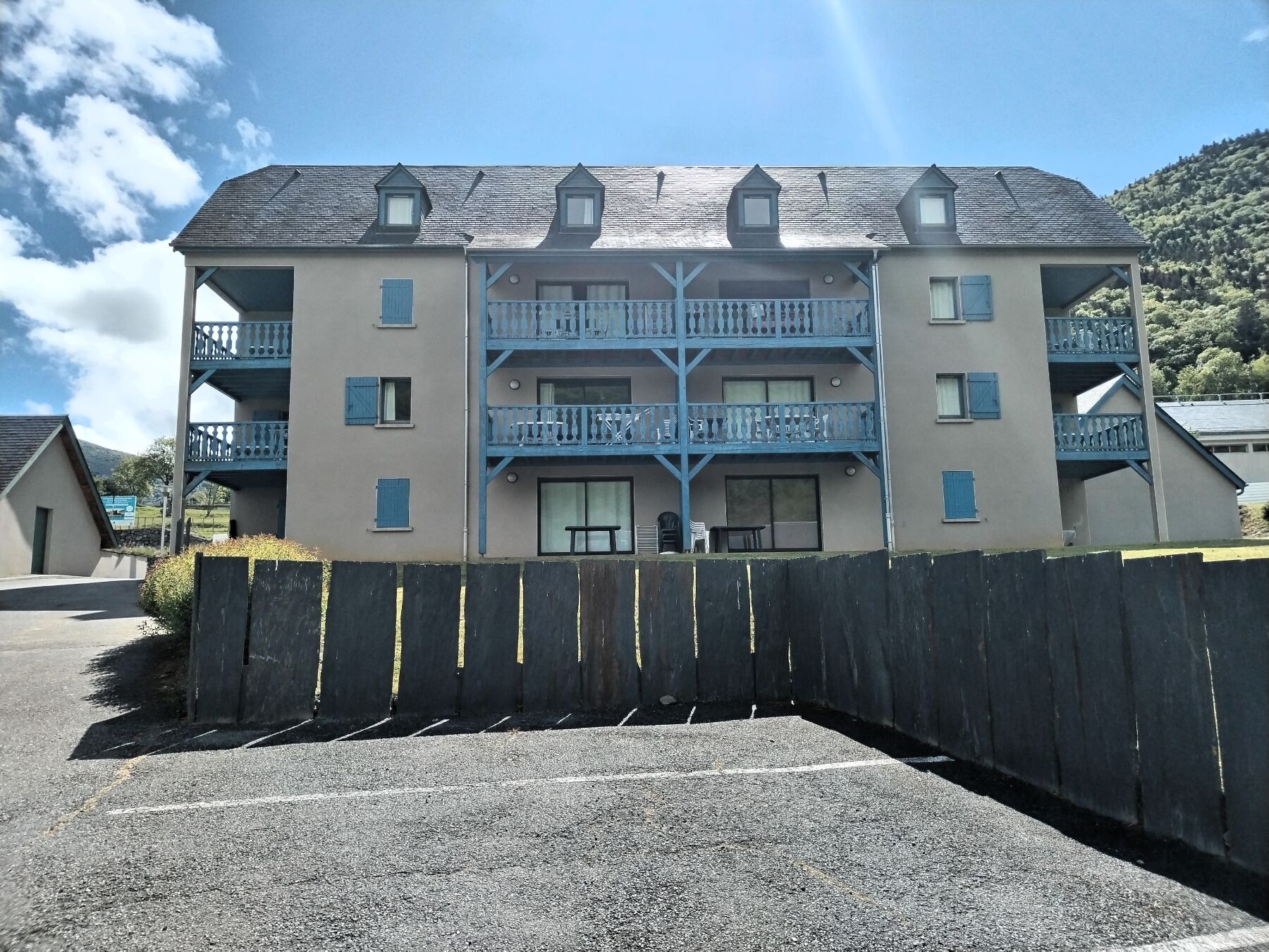 Un immeuble à plusieurs étages doté de balcons, d’un espace de stationnement et d’une clôture.