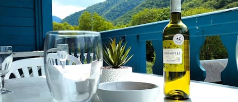 Une table avec une bouteille de vin, un saladier et des verres à vin, sur une terrasse offrant une vue sur des collines verdoyantes.