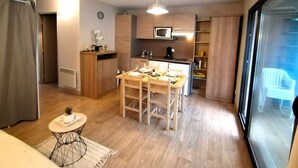A compact kitchen with modern appliances, a dining area with a table and chairs, and a large sliding glass door leading to a balcony. - Arreau, Apt: 1-bedroom apartment with terrace and pool, Lake Génos (Arreau)