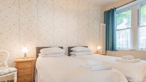 A bedroom with two beds, a nightstand with a lamp, a chair, and a window with curtains. - 2 Bed in Keswick (oc-sz215) (Keswick)