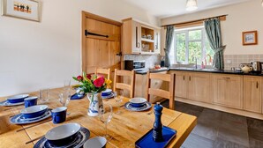 Een eetgedeelte met een houten tafel voor vier personen, een keuken met houten kastjes en een raam met gordijnen.