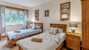 Een slaapkamer met twee bedden, een raam met gordijnen, een nachtkastje met een lamp en een garderobe.