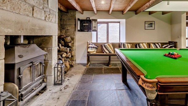 Een gezellige kamer met een stenen openhaard, een biljarttafel en een bank met streepkussens.