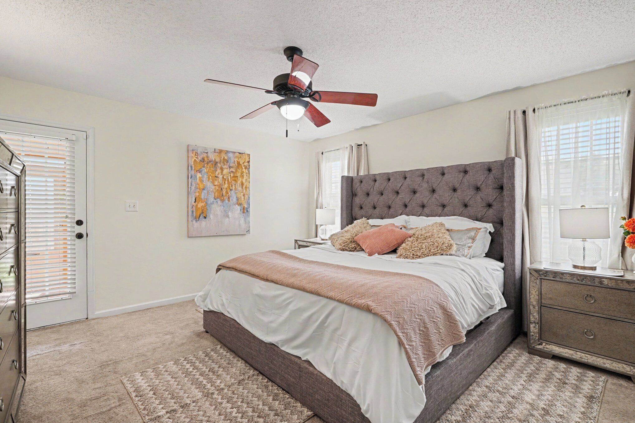 A bedroom with a bed, a ceiling fan, a nightstand, a dresser, and a painting on the wall.