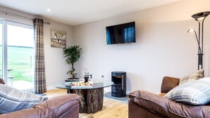 Ein modernes Wohnzimmer mit Ledersofas, einem Couchtisch, einem Flachbildfernseher, einem Kamin und einem großen Fenster mit Vorhängen.