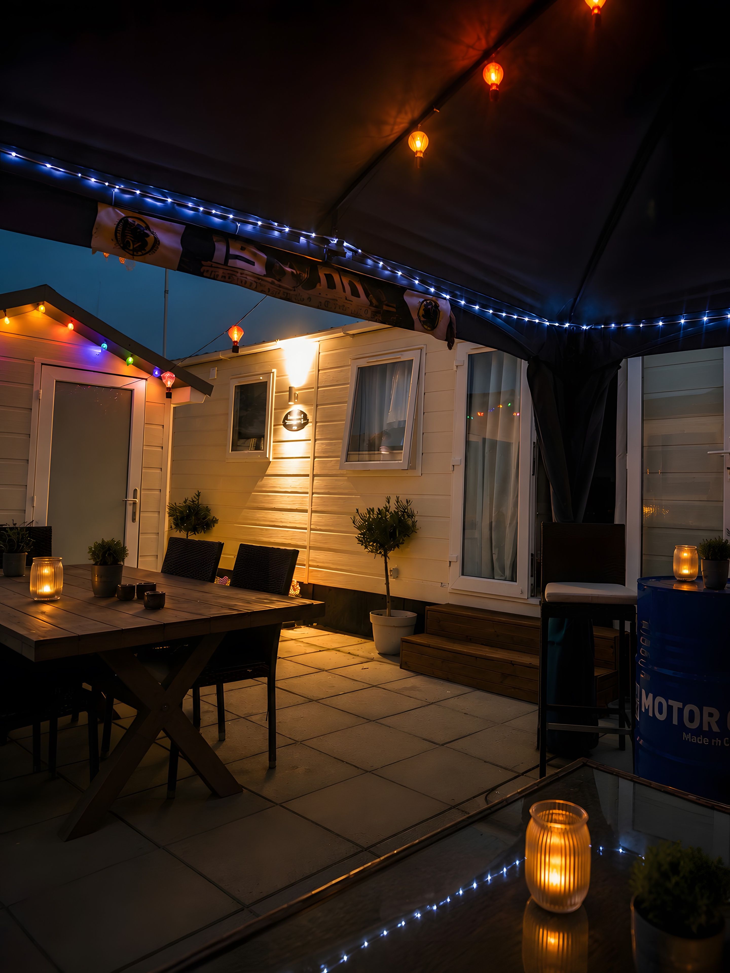 Een overdekt terras met een eettafel, stoelen en lichtjes.