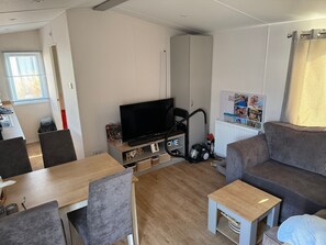 A living room with a TV, sofa, and a small table. - Chalet 'Duinzicht' with Shared Pool, Private Garden and Wi-Fi (Kamperland)