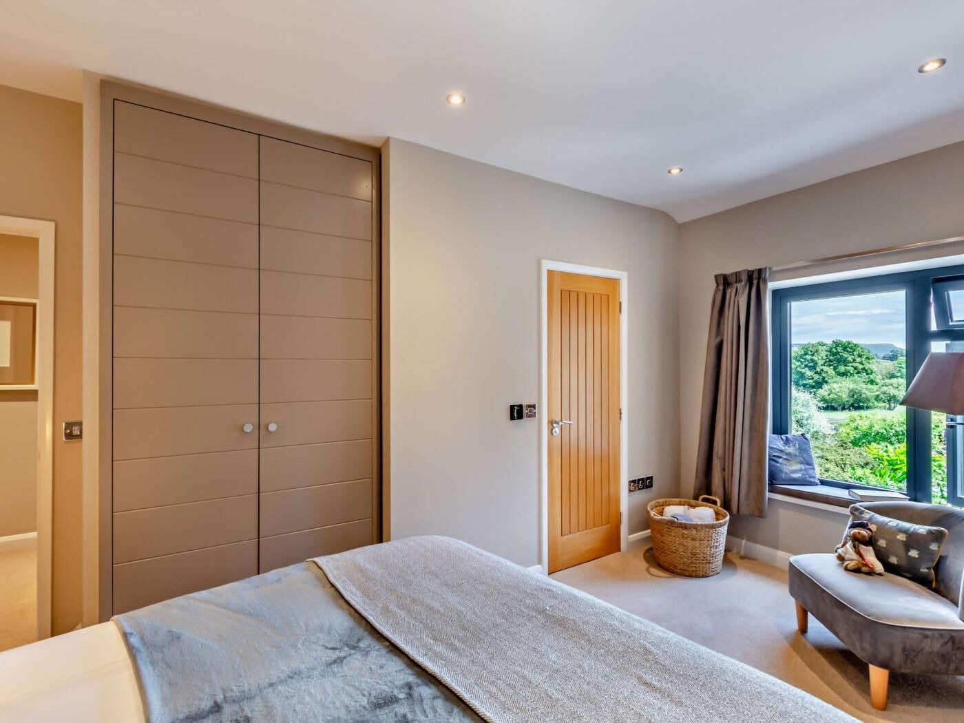 A bedroom with a bed, a wardrobe, a door, a window with a view, and a small seating area.