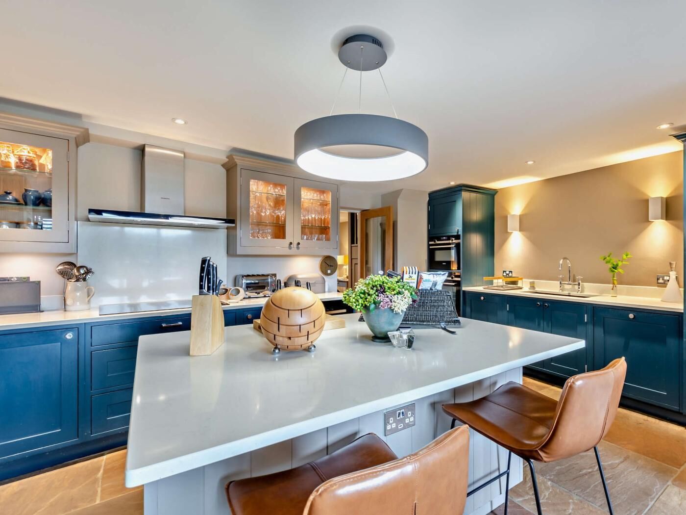Une cuisine moderne avec un îlot central, des meubles de couleur bleu foncé et un luminaire suspendu.