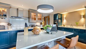 Et moderne køkken med en central ø, mørkeblå skabe og en hængende lampe.