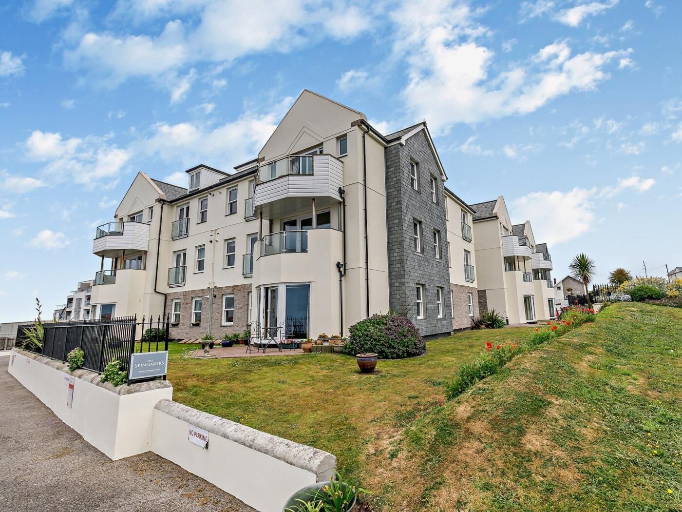 A multi-story residential building with balconies, a landscaped garden, and a 'NO PARKING' sign.