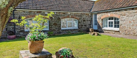 A stone building with a tiled roof, a grassy yard, and flower planters.