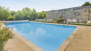 Una piscina rectangular al aire libre con un muro de piedra y sillones de descanso a un lado.