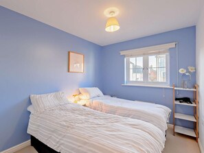 A bedroom with two beds, a window with a view, a bedside table, and a shelf with flowers. - 3 Bed in Camber (oc-bt011) (Camber)