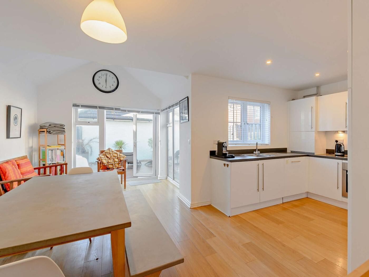 A modern kitchen with white cabinets, a dining area with a table and chairs, and a view through the glass doors.
