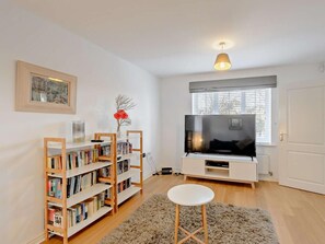 A living room with a TV, bookshelf, and a small white stool. - 3 Bed in Camber (oc-bt011) (Camber)
