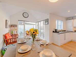 A dining area with a table set for four, a clock on the wall, and a view through a glass door. - 3 Bed in Camber (oc-bt011) (Camber)