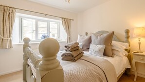 A bedroom with a bed, pillows, a bedside table, a lamp, and a window with curtains. - 2 Bed in Cheltenham (oc-46677) (Bourton-on-the-Water)