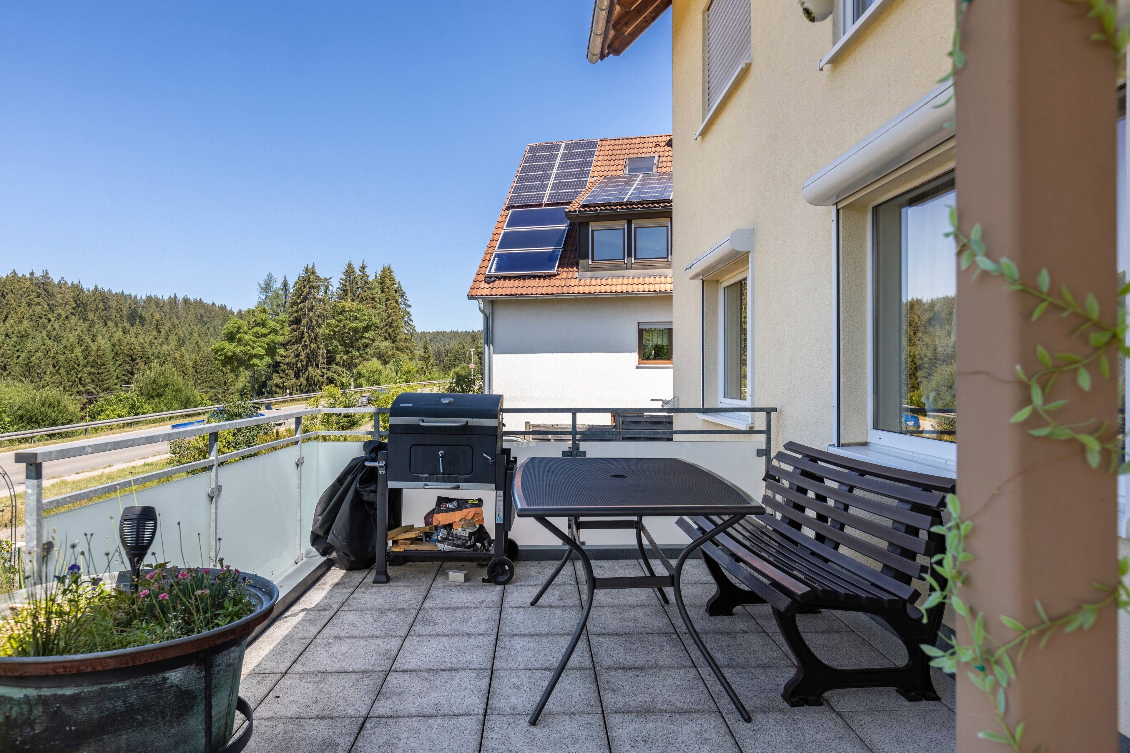 Een balkon met een barbecue, een tafel en een bank.