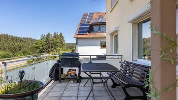 Een balkon met een barbecue, een tafel en een bank.