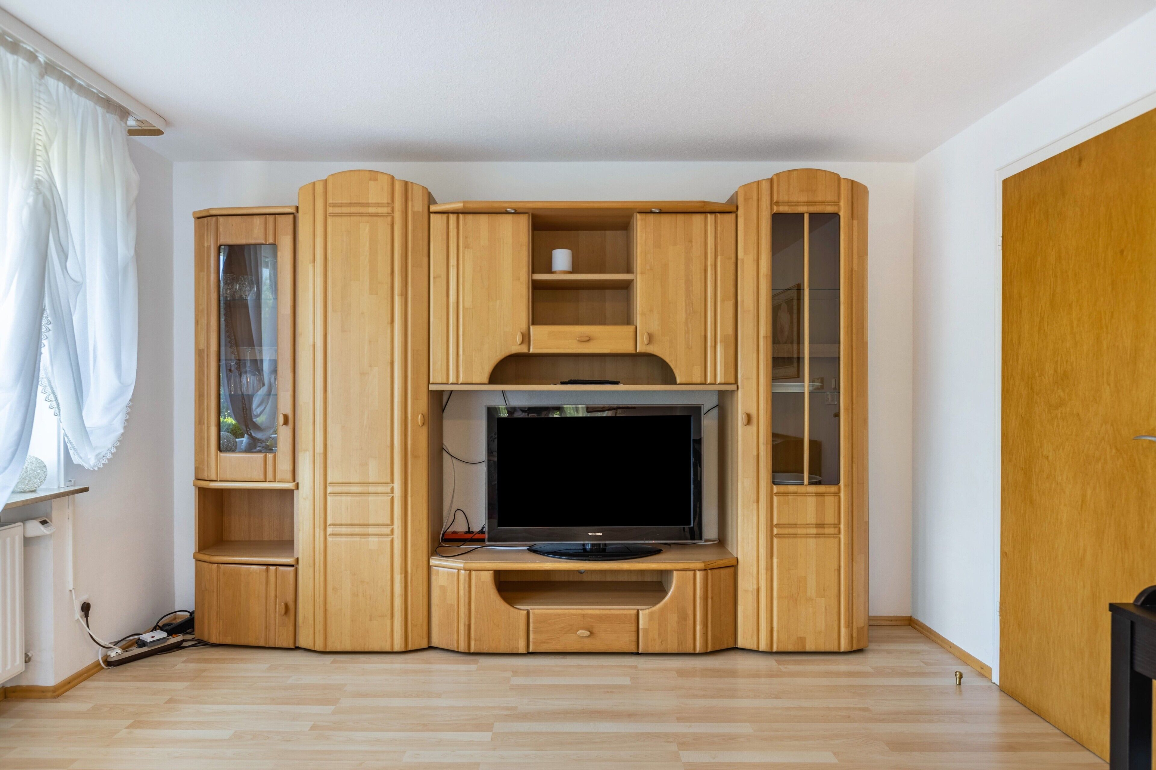 A compact wooden entertainment unit with a flat-screen TV, shelves, and a small cabinet.