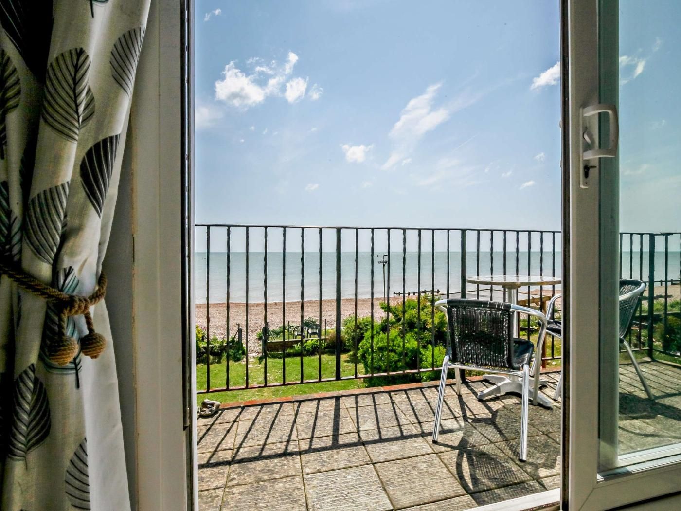 A balcony with a view of the beach, a chair, and a table.