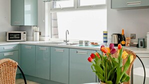 Una cocina moderna con gabinetes color turquesa, microondas, pileta y ventana con cortinas estampadas.