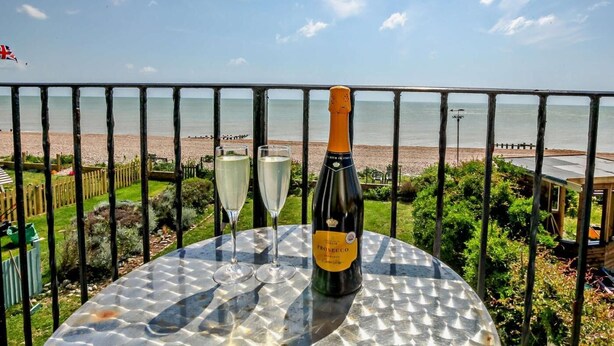 Una mesa con una botella de Prosecco y dos copas, con vista a una playa.