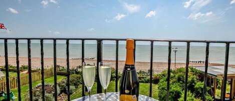 Une table avec une bouteille de Prosecco et deux verres, donnant sur une plage.