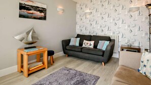 Una sala de estar con un sofá, una mesita de madera, un tapete y una pared con estampado de velero.
