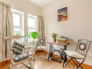 Ein gemütliches Zimmer mit einem Schaukelstuhl, einem weißen Stuhl, einem Tisch mit einem Korb und einer Nähmaschine.