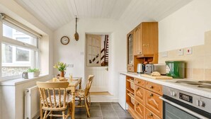Una cucina con mobili in legno, un tavolo da pranzo con sedie, un termosifone e una sveglia appesa al muro.