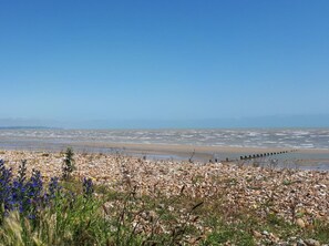 Een kustlandschap met een rotsachtige voorgrond, een zandstrand en een helderblauwe lucht.