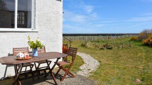Uma casa branca com janela, uma mesa de madeira com cadeiras e um jardim com cerca.