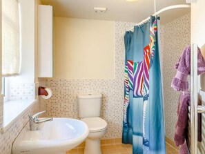 Ein Badezimmer mit einem weißen Waschbecken, einer Toilette, einem farbenfrohen Duschvorhang und einem violetten Handtuch auf einem Ablagekorb.