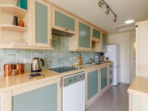 Eine Küche mit hellen Holzschränken, einer gefliesten Spritzschutzwand, einem Geschirrspüler und einem Kühlschrank.