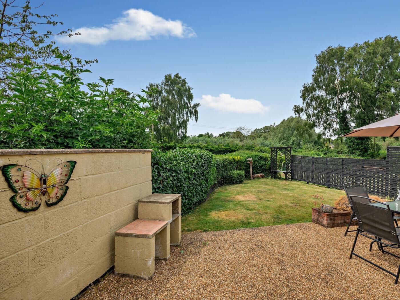 A backyard with a concrete wall, a butterfly decoration, a bench, a grill, and a table with chairs.