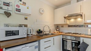Una cocina compacta equipada con microondas, hervidor eléctrico, pileta, estufa, horno y un reloj en la pared.