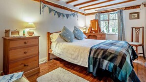 Een slaapkamer met een houten plafond, een bed met een geruite deken, een dressoir, een lamp en een raam met gordijnen.