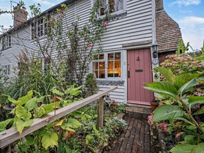 Ein weißes Holzhaus mit roter Tür, einem Ziegelweg und verschiedenen Pflanzen.