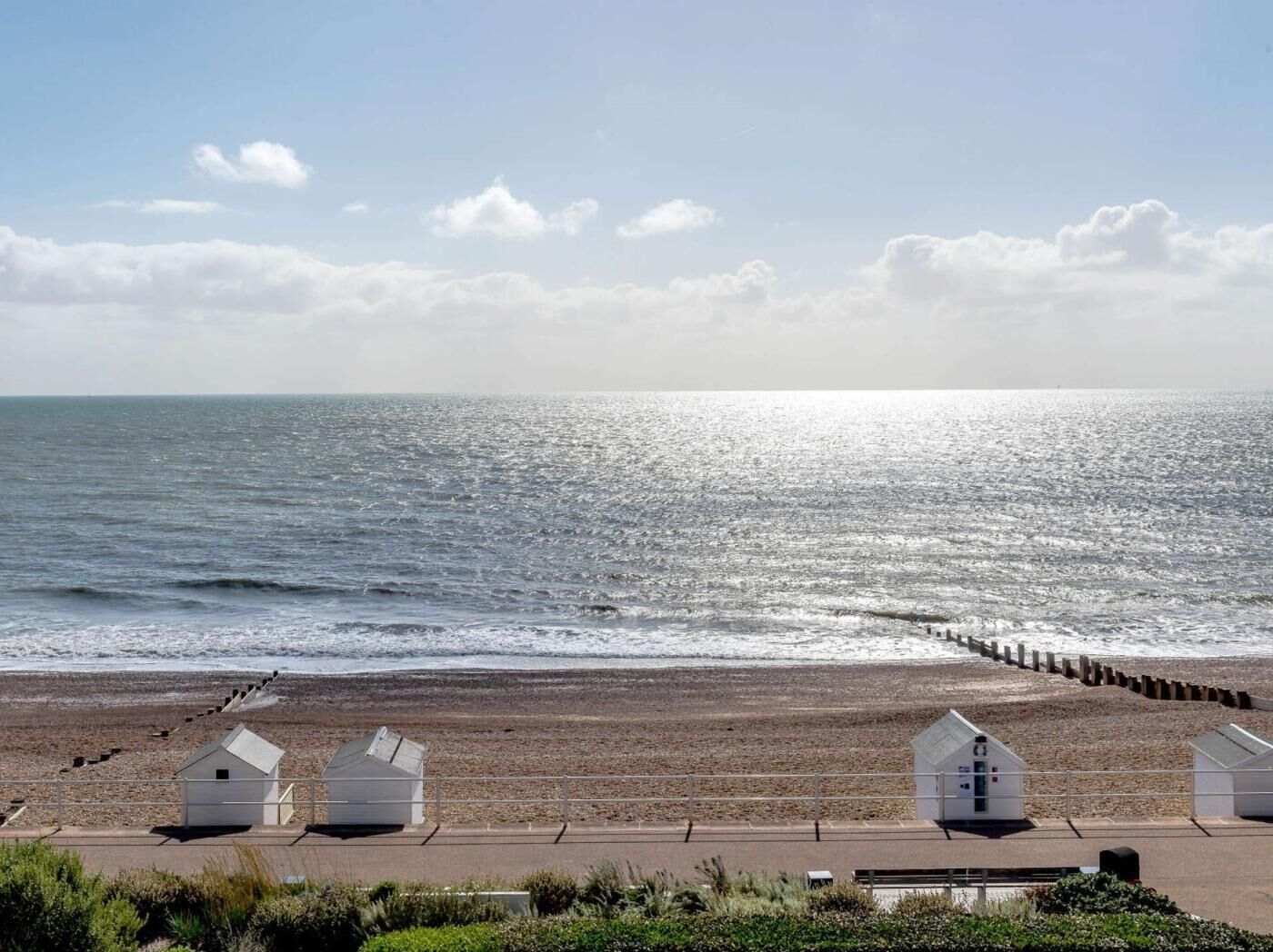 A beach with a wooden pier, white beach huts, and a clear sky.