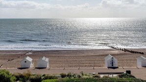 A beach with a wooden pier, white beach huts, and a clear sky. - 3 Bed in Bexhill On Sea (oc-bt037) (Bexhill-on-Sea)