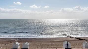 A beach with a wooden pier, white beach huts, and a clear sky.