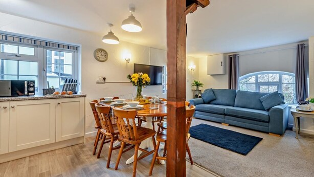 A modern kitchen with wooden chairs, a dining table, and a large wooden pillar. - 4 Bed in Bideford (oc-46840) (Pusehill)