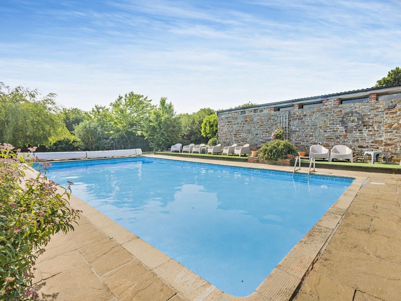 A rectangular swimming pool with a stone wall and white chairs along its edge.
