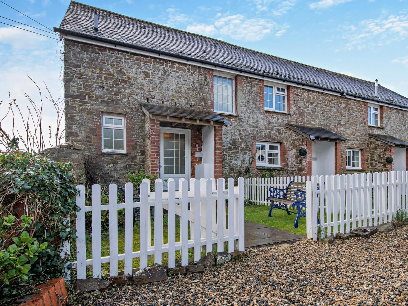 A stone building with a white picket fence, a bench, and a gravel driveway.